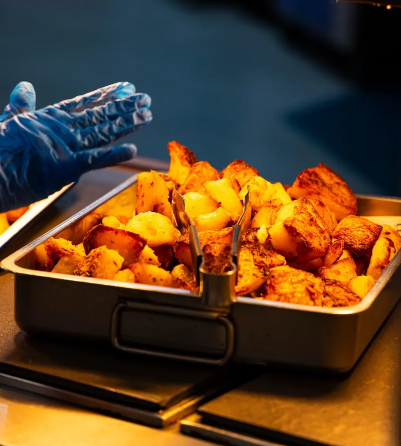 A TNINE chef serving roast potatoes at the hot counter