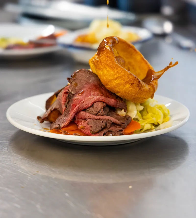 Roast beef with a Yorkshire pudding, gravy being poured on the pass in the TNINE kitchen