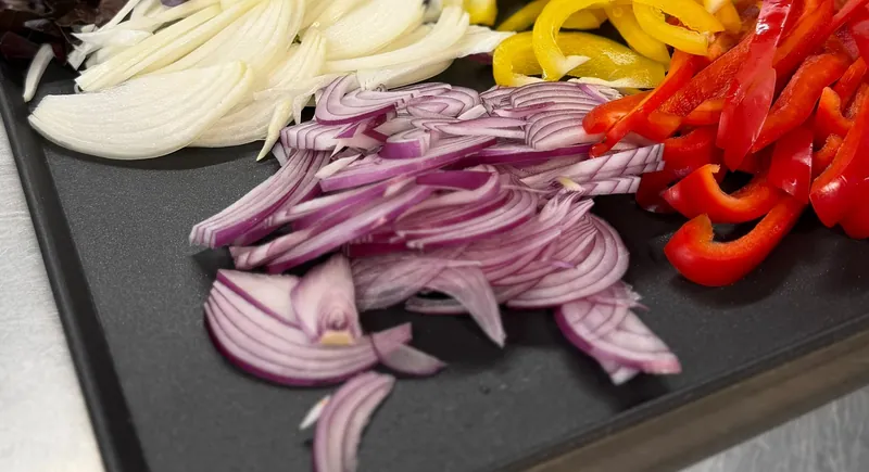 Peppers, red onion and white onion sliced by hand on a prep tray