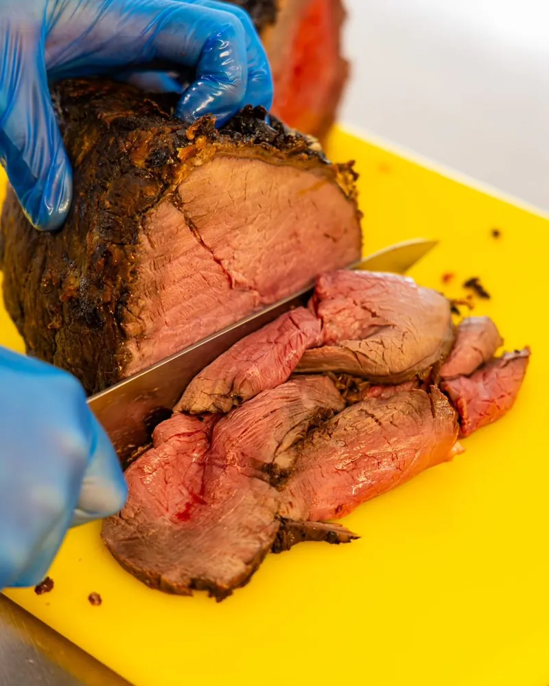 Roast beef being carved into slices on a yellow board