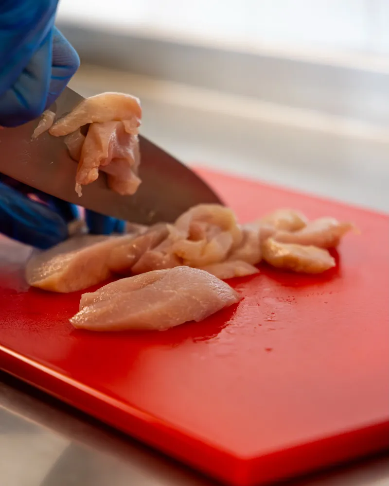 Chicken breast sliced by hand on a red chopping board