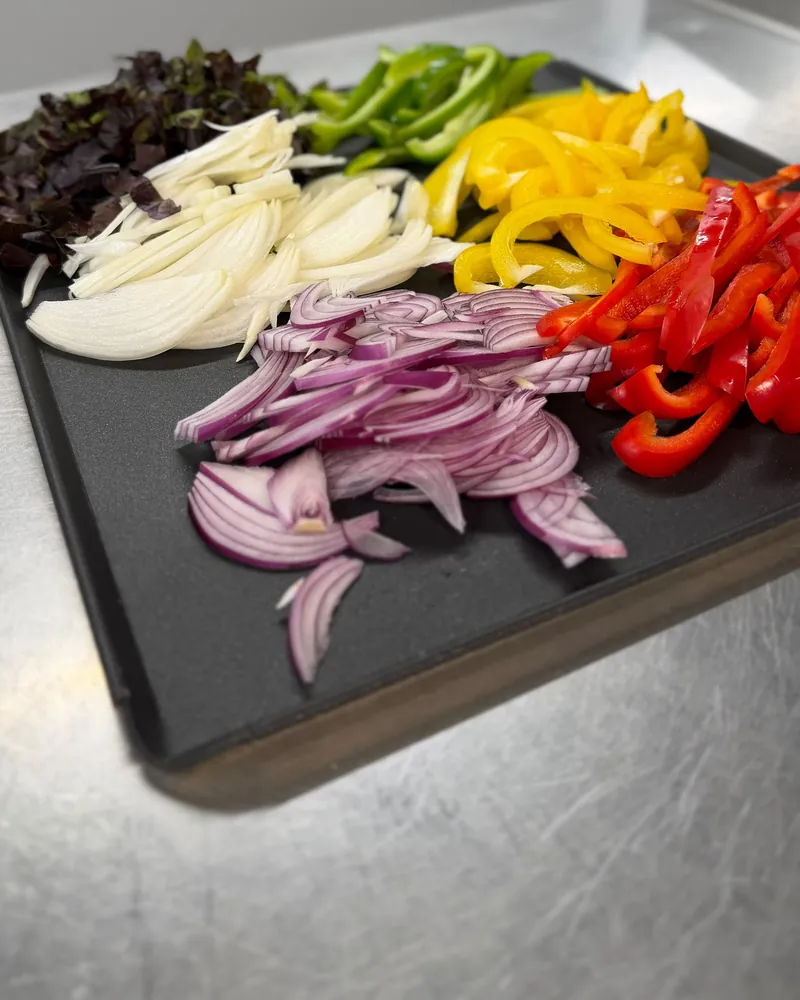 Peppers, red onion and white onion sliced by hand on a prep tray
